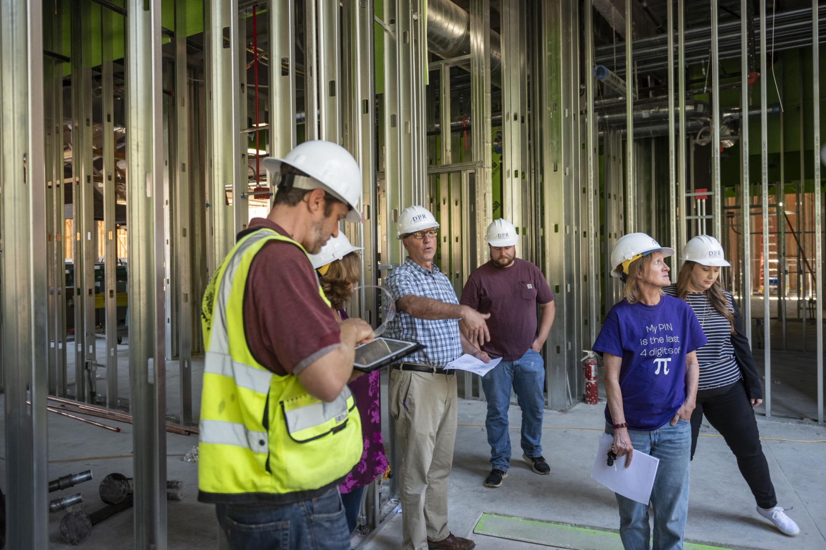 Randy Miller gestures as others in hard hats walk through the interior steel framed walls of the building.