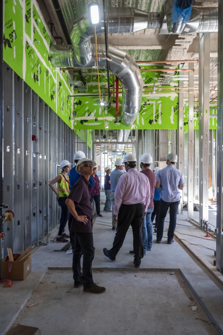 A group of people in hardhats stands in the hallway of the new building, which has construction materials scattered about.
