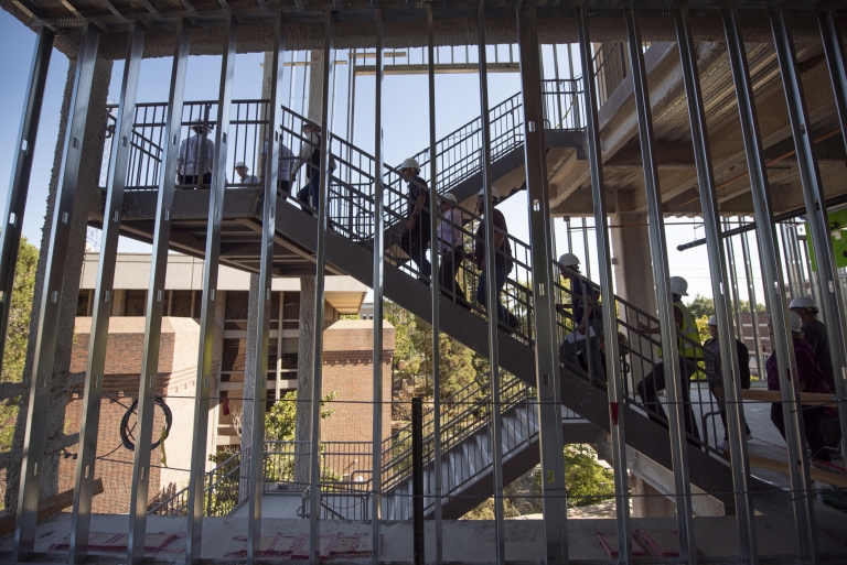 People climb the exterior staircase of the new building, as seen through the steel-framed walls.