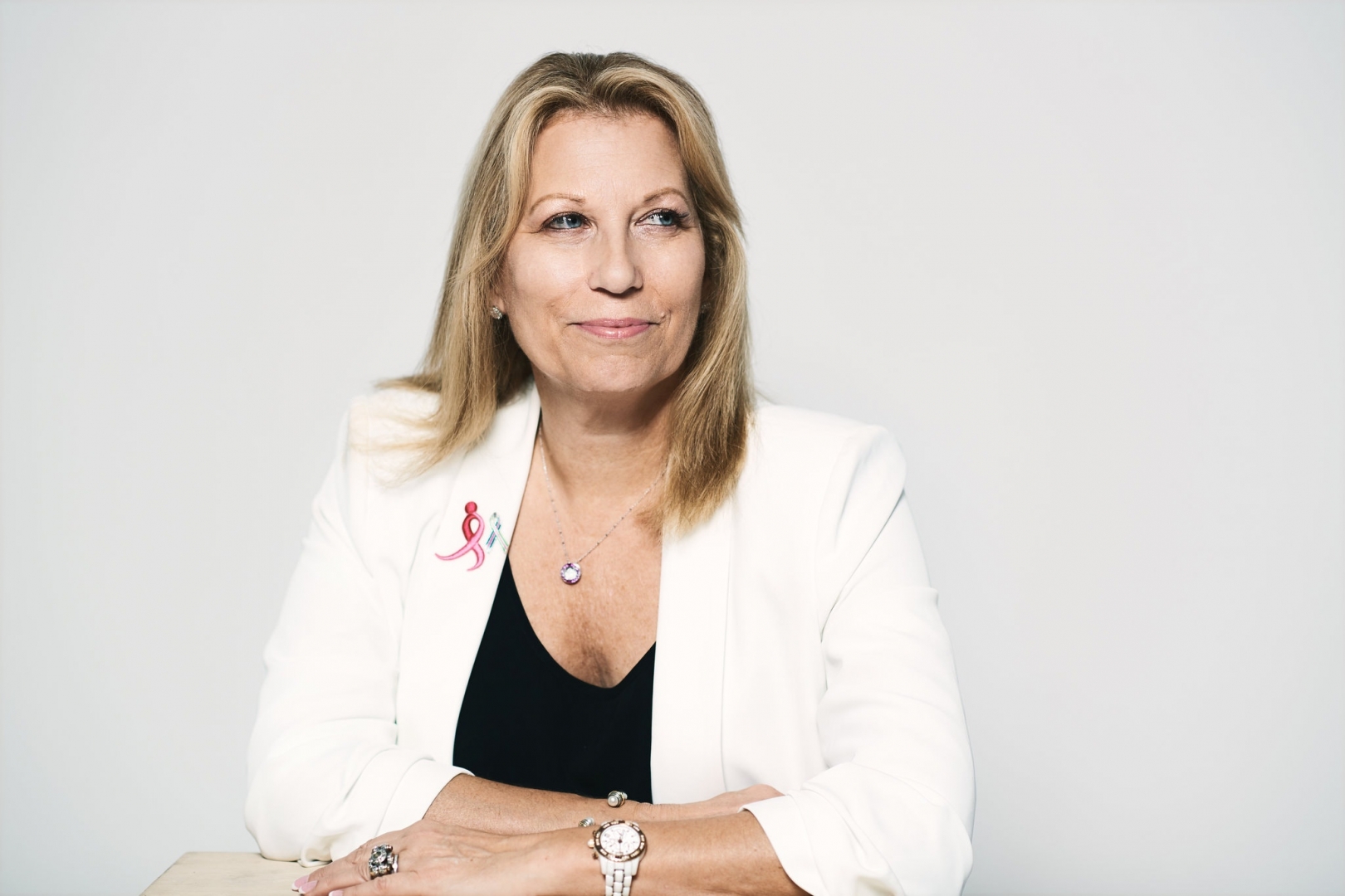 Portrait of Paula Schneider in a white blazer with pink ribbon lapel pin.