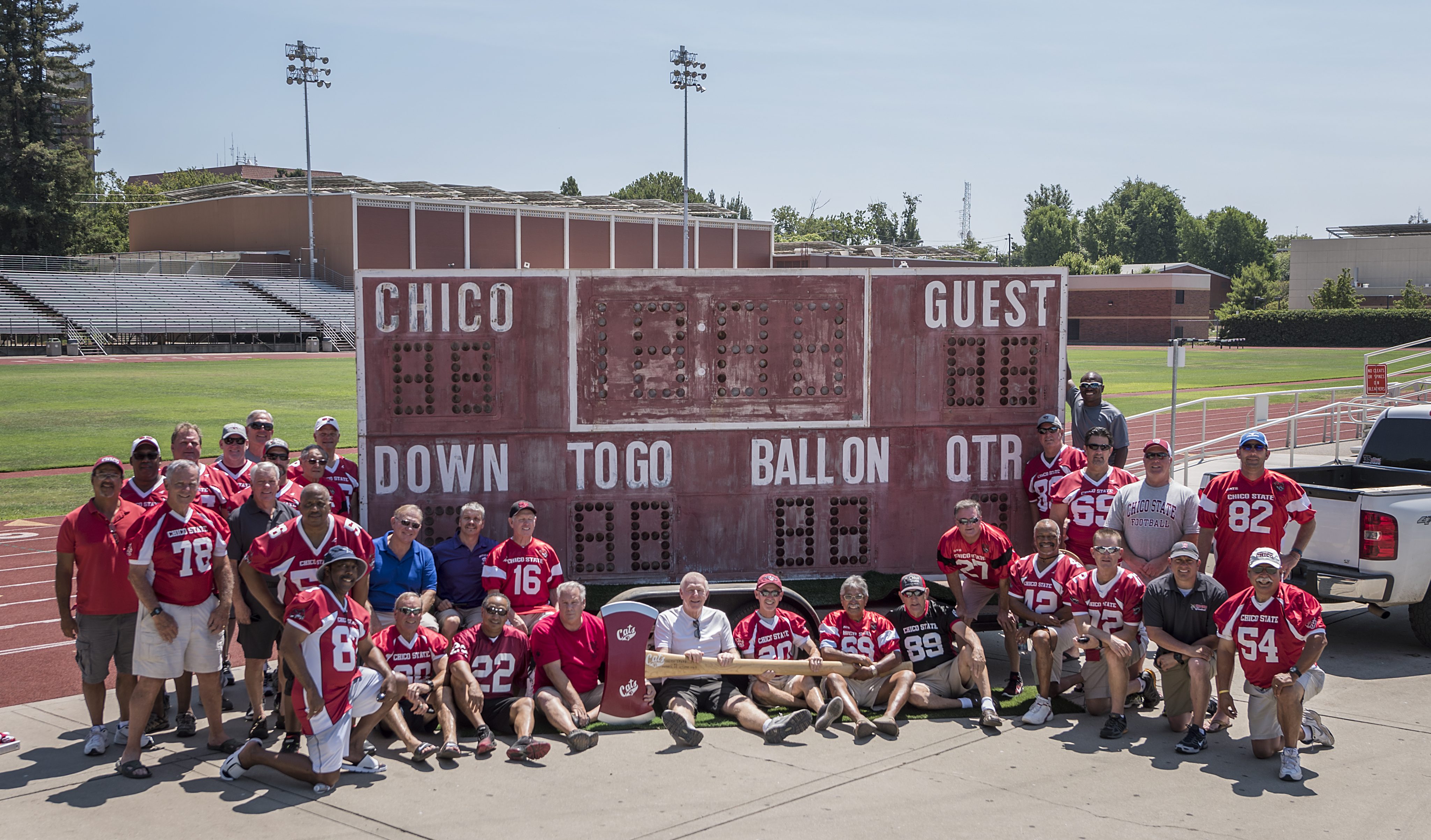 Alumni of the Chico State football team pose next to the old scoreboard.