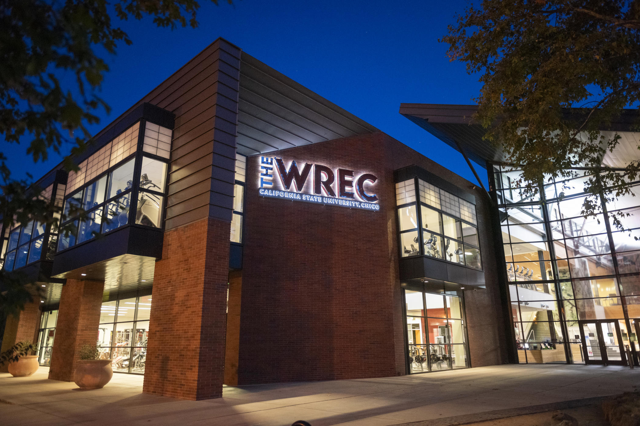 The WREC sign is illuminated at night, with views of the workout equipment visible through the windows.