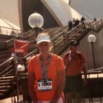 Vanden Bosch wearing running clothes, race bib, and a medal sits in front of the Sydney Opera House