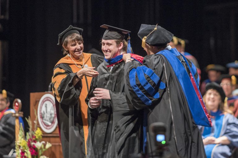 MBA graduate receives his master's hood from two faculty