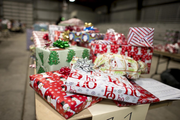 A stack of wrapped holiday gifts sits on a table.
