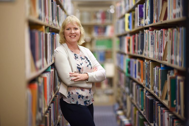 Corina Yetter leans against a shelf of books in the Meriam Library.