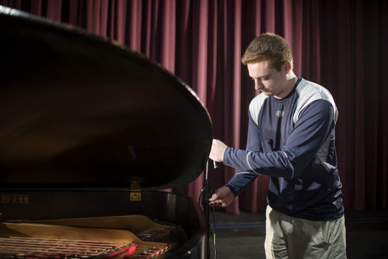 Kyle Bailey sets up audio equipment for a grand piano