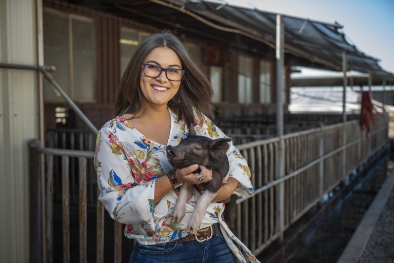 Megan Rivera holds a piglet in her arms and scratches it under its chin outside the swine unit.