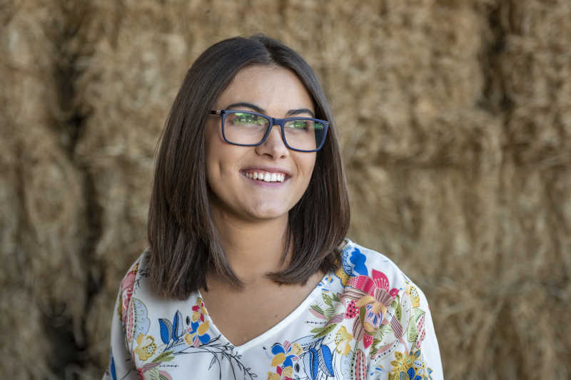 Portrait of Megan Rivera in front of some hay bales.