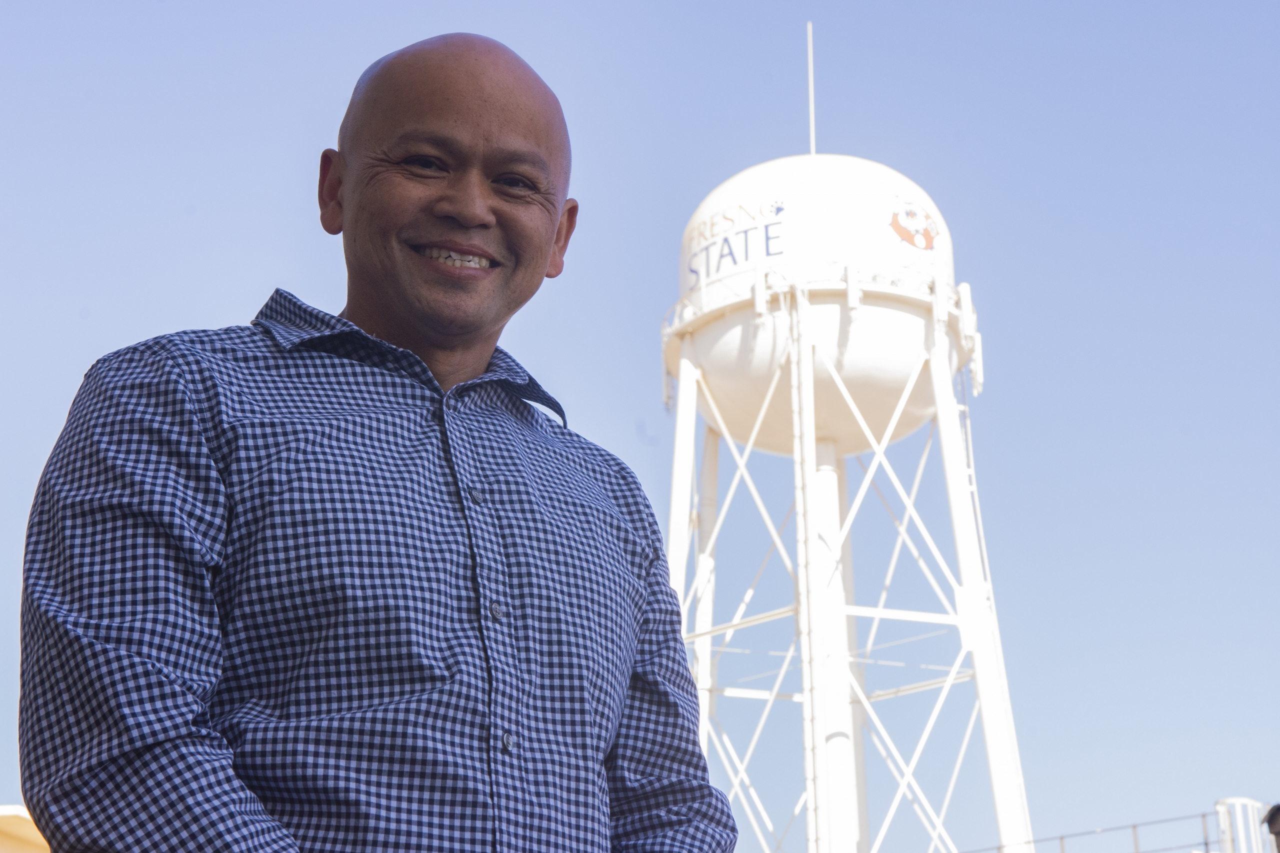 Neil Tung poses and smiles with a water tower standing tall behind him.