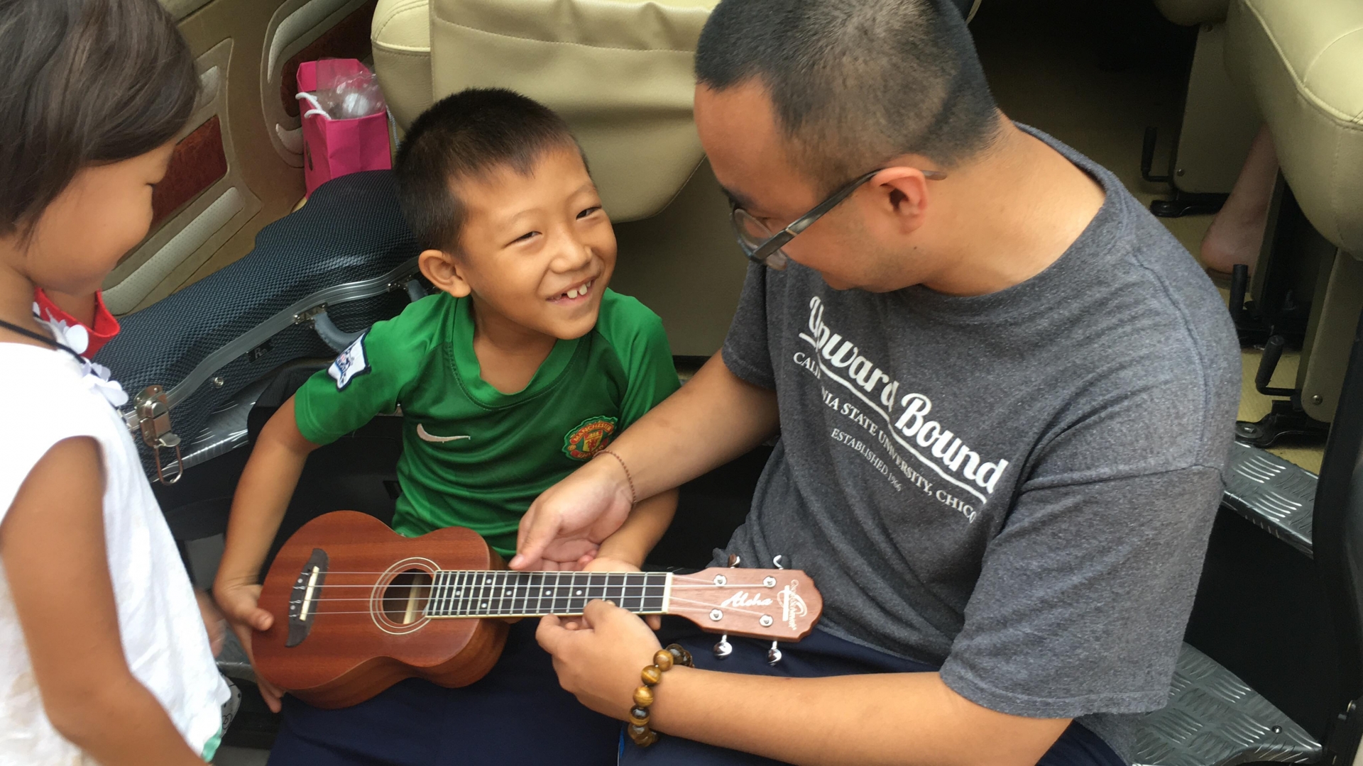 Pengcheng plays a small string instrument with a young boy.