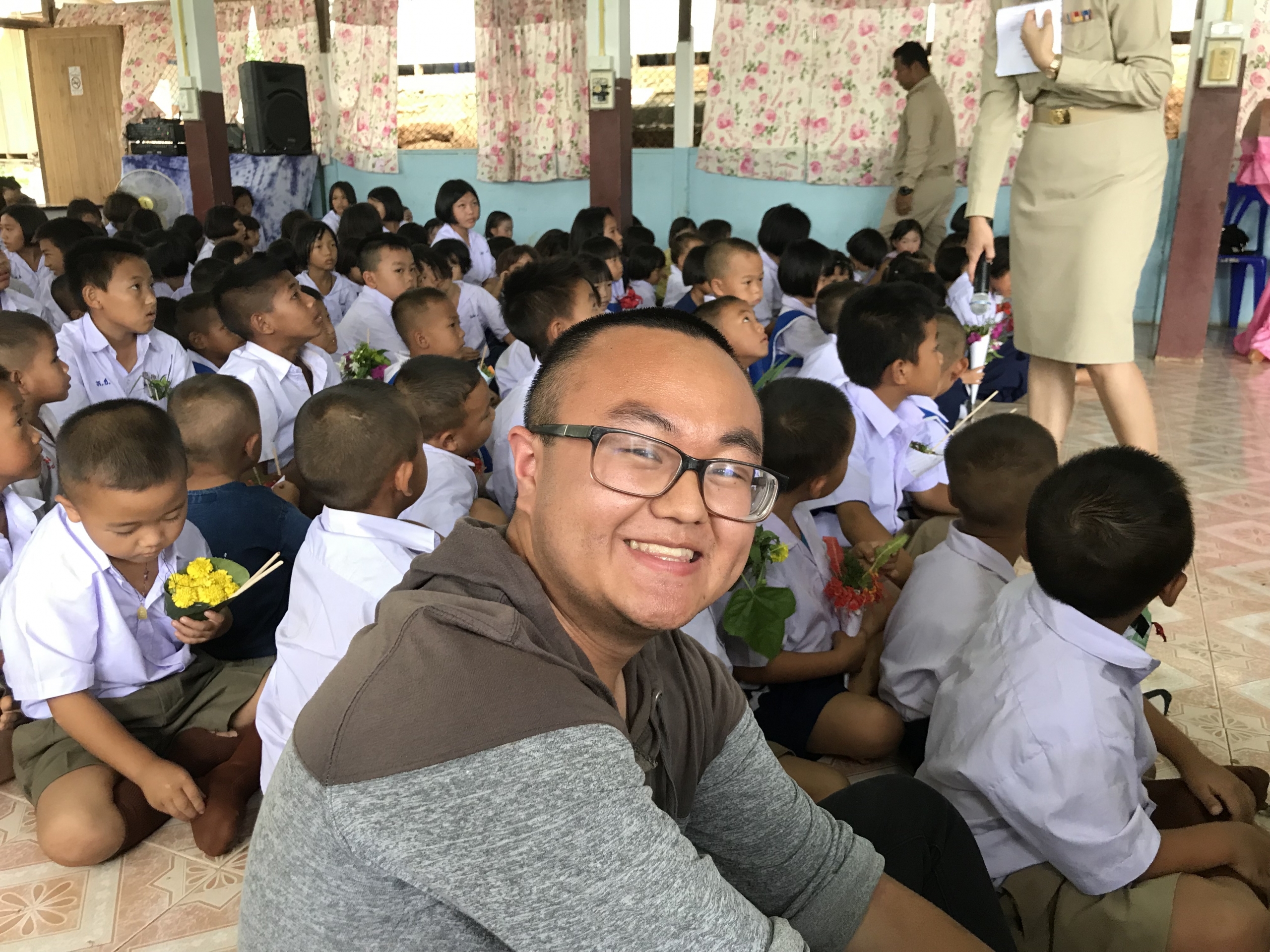 Pengcheng sits on the floor of a classroom surrounded by small children in uniform.