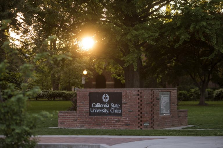 The sun sets behind the University sign on the Kendall Hall lawn on an early mid-spring evening.