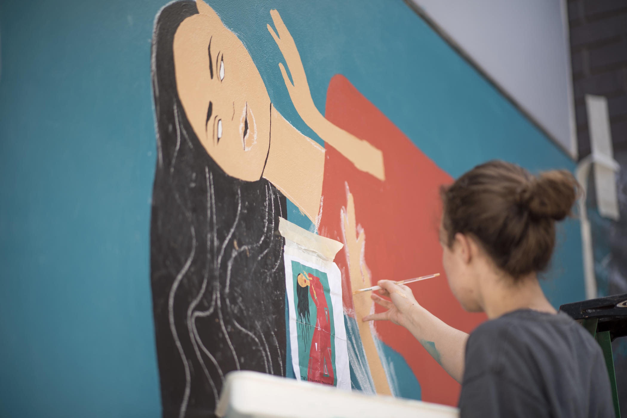 Autumn Robertson paints a mural of a woman on a campus wall.