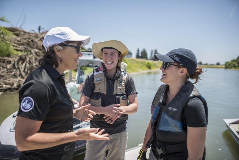 President Gayle Hutchinson laughs with graduate students Valerie Sgheiza and Mallory Peters as they stand on a dock on the Sacramento River.