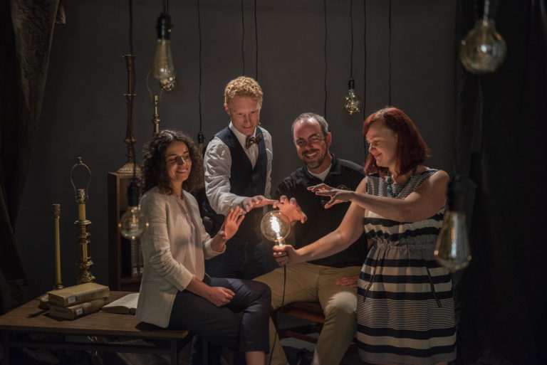 a group of four faculty gather around a lit lightbulb