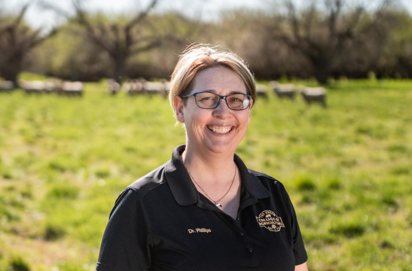 Portrait of Celina Phillips with sheep in a field behind her.