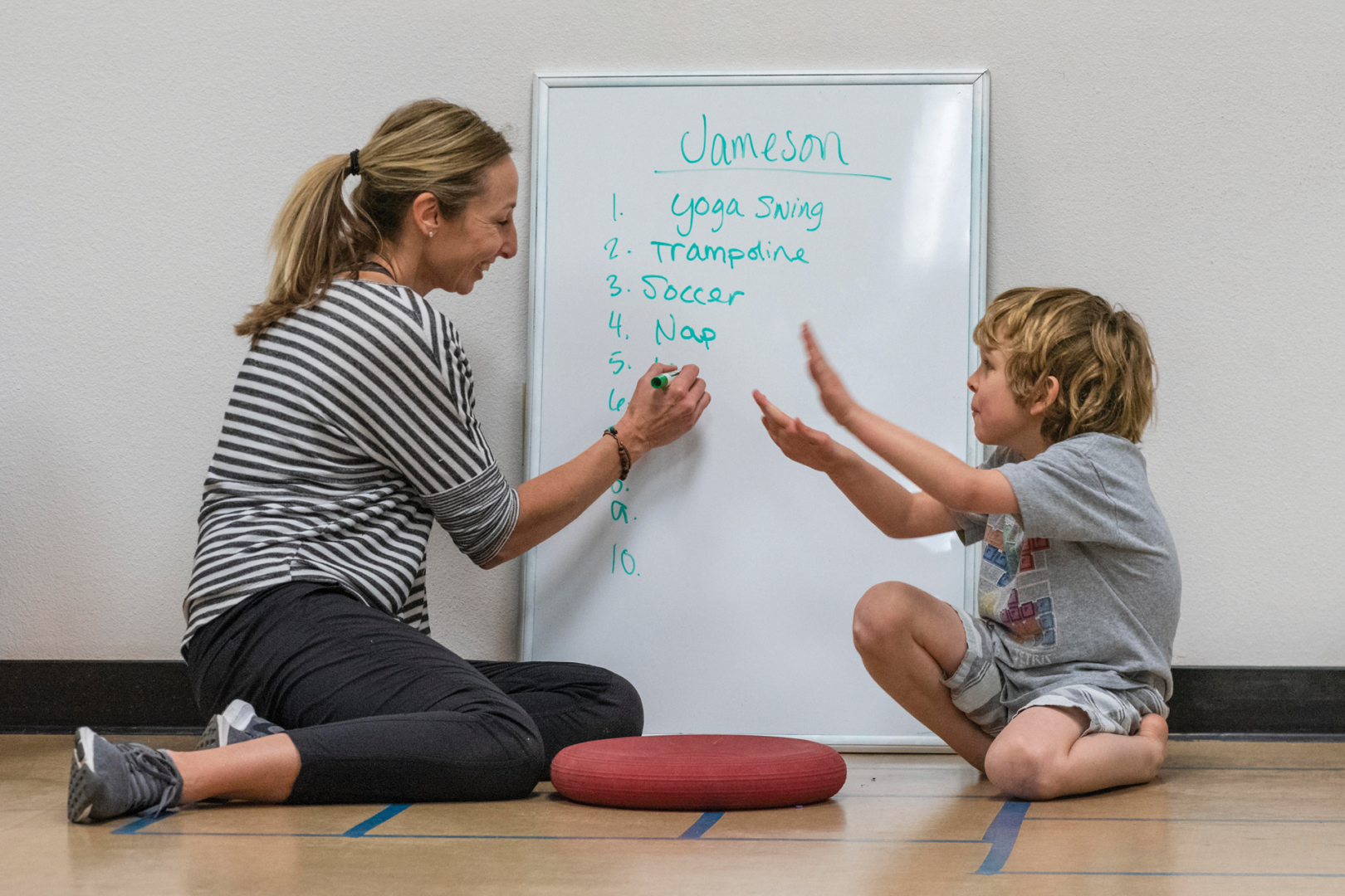 A clinician and a boy make a list of activities to do in the autism clinic, such as yoga swing, trampoline, soccer, and nap.