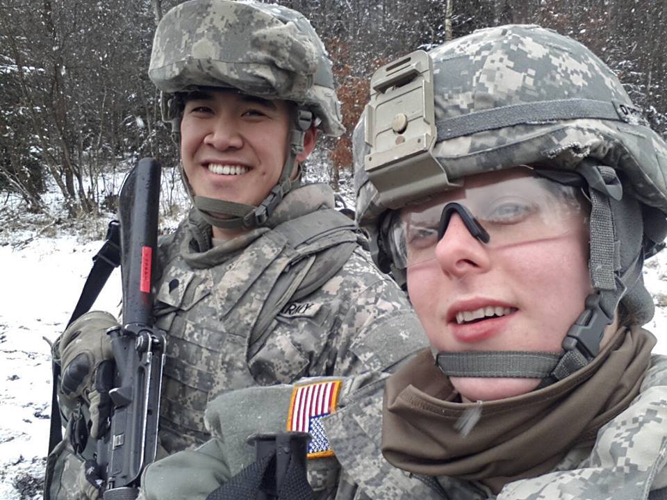 Bryan Lewis (left) and an unidentified Army soldier smile for the camera, wearing fatigues and helmets.