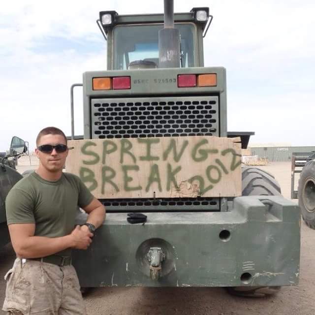 Jason Blum smiles as he leans on heavy machinery with a sign reading "Spring Break 2012."
