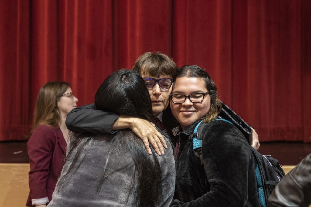 President Hutchinson hugs close two people on either side of her inside the BMU Auditorium