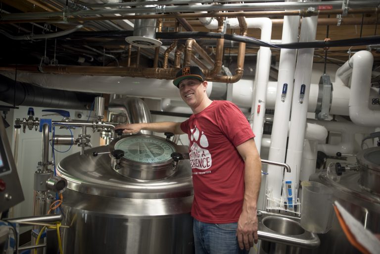 Josh Leavy smiles as he brews Resilience IPA in a container reading "San Francisco Brewing Co."
