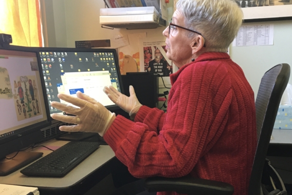 A woman speaks toward her computer while wearing rubber gloves.
