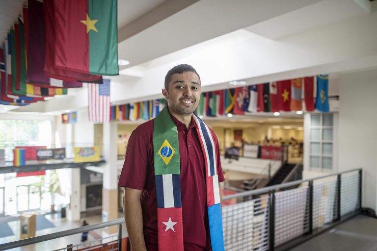 Marco Macotela stands on the second floor of the BMU with flags from around the world behind him.