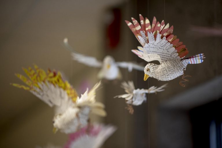 Small sculptures of flying birds, made out of book pages and colored paper, hang from the ceiling.