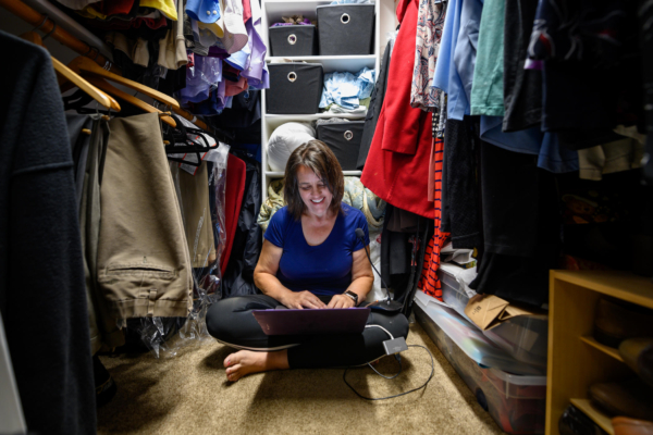 Marianna Paiva smiles as she works on her laptop on the floor of her closet.