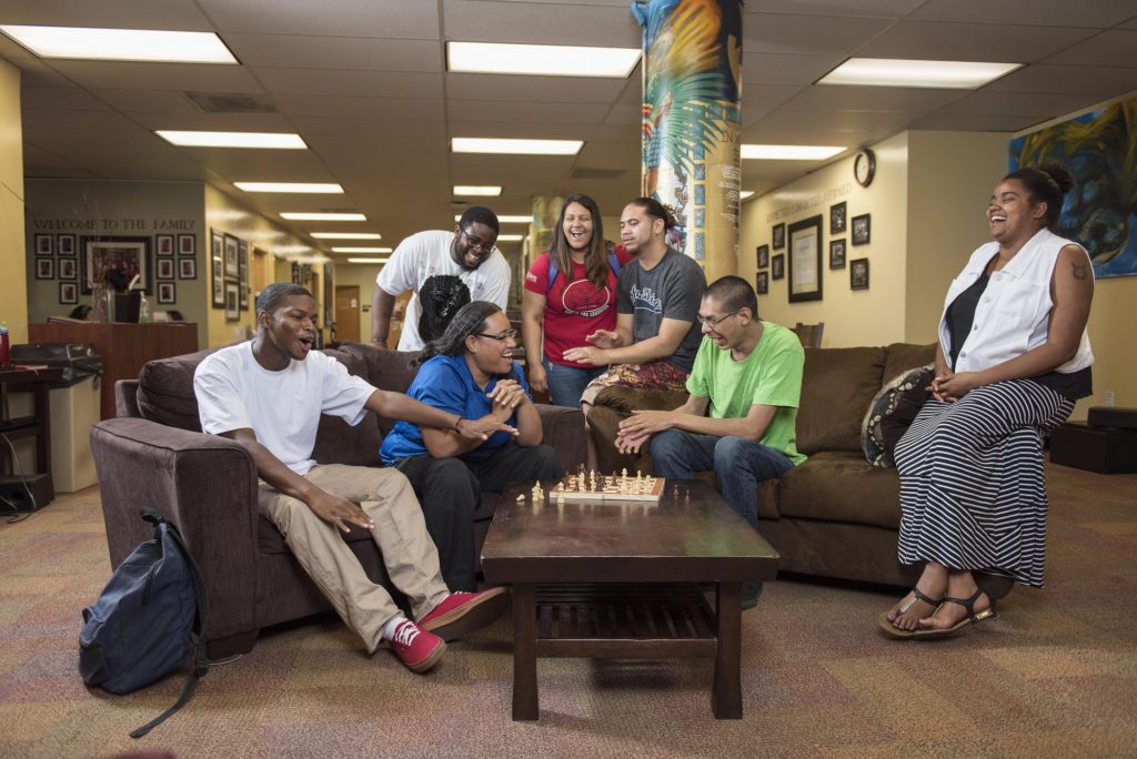 A group of students gather on couches in the CCLC and play chess on the coffee table.