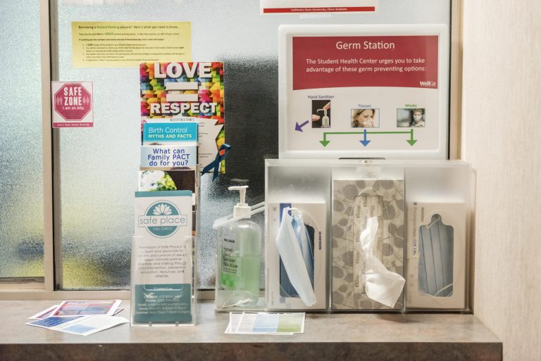 Information pamphlets, hand sanitizer, and boxes of face masks and issues sit on a counter.