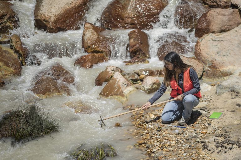 Angelica Rodriguez leans over a stream and collects a water sample.