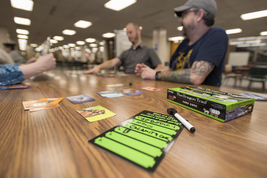 Image of game pieces on a table with players talking in the background.