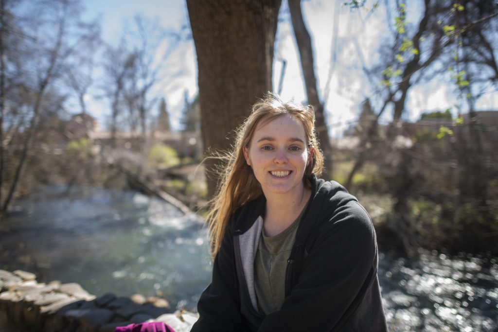 Caitlin Davis sits beside a flowing creek on campus on a sunny day.