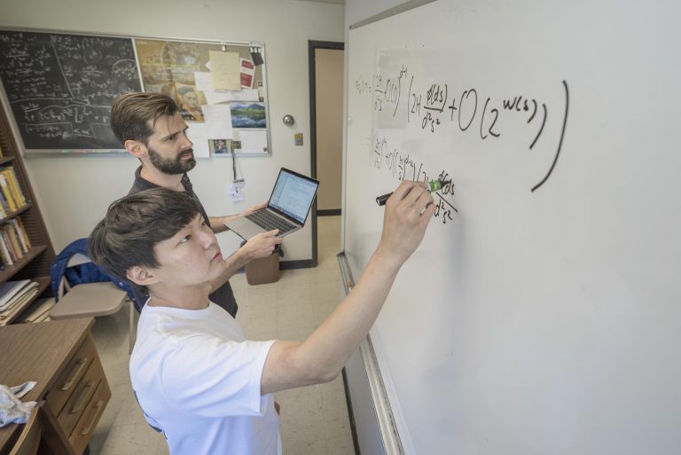 Jongwoo Choi and faculty Kevin McGown work out math problems on a white board.