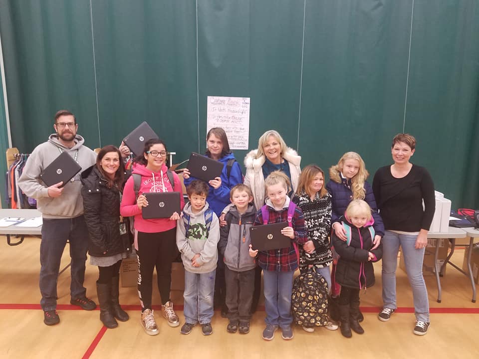 Brian Ausland and wife Jodi Halligan pose with a group of young students holding laptops. 