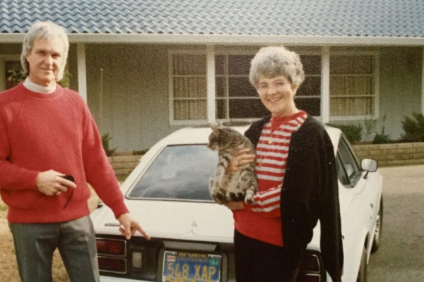 Ladd Johnson and a woman holding a cat stand next to a car outside a home.