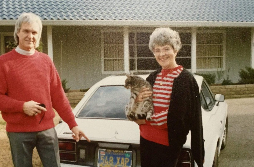 Ladd Johnson and a woman holding a cat stand next to a car outside a home.