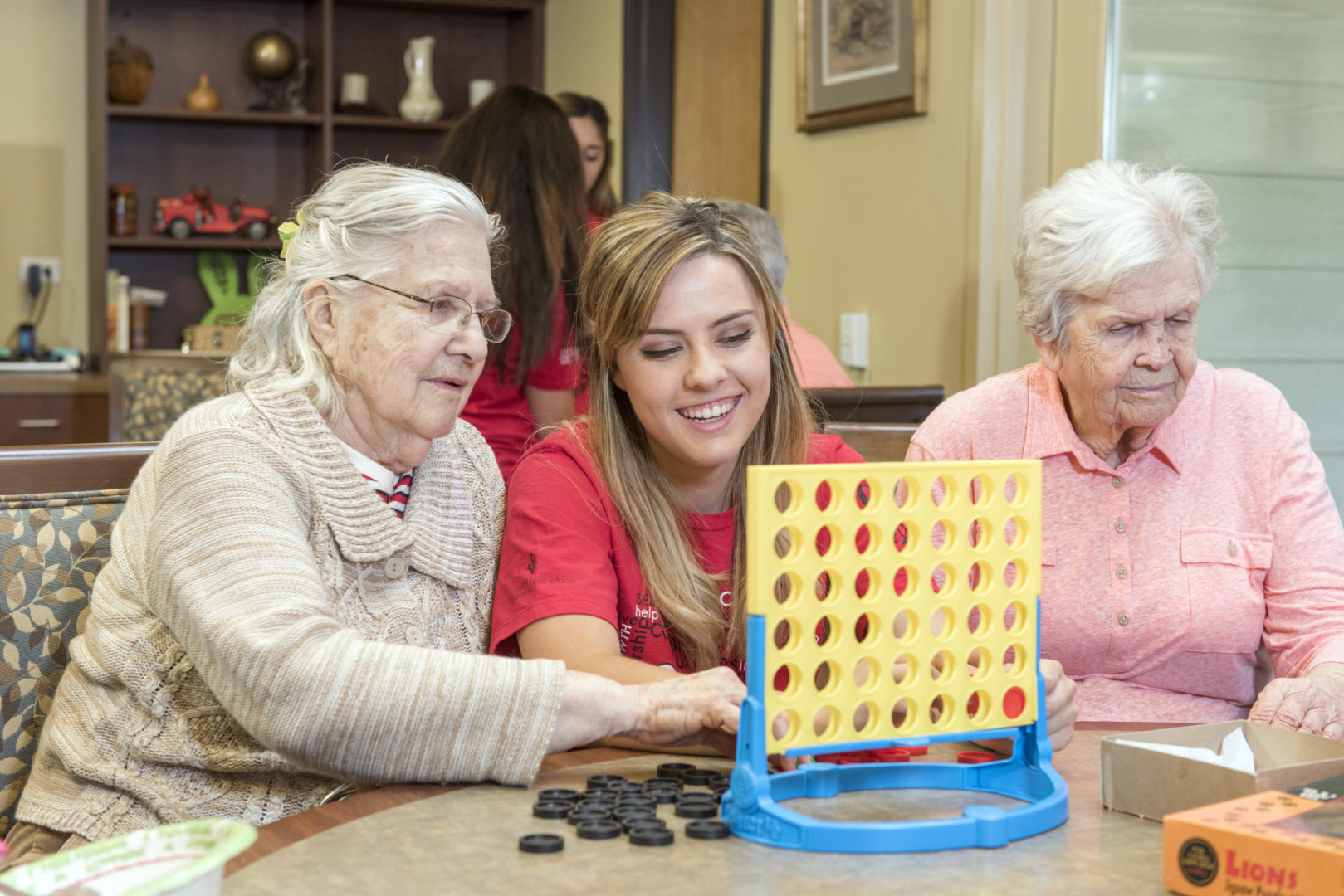 A student plays Connect Four with senior citizens at an assisted living facility.