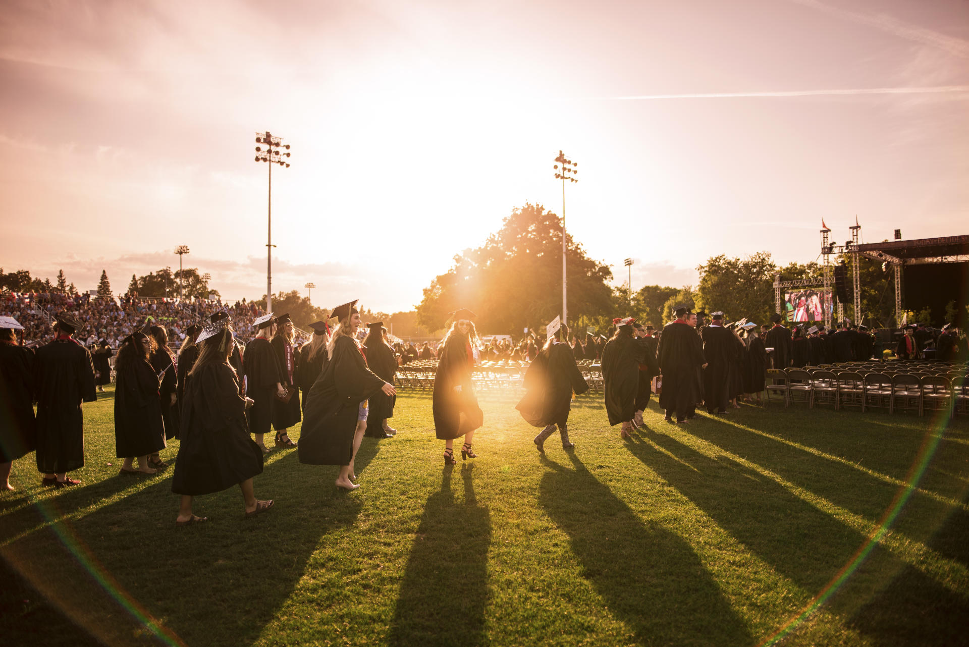 New;ly graduated students return to their seats after receiving their diplomas in front of a sunset backdrop.
