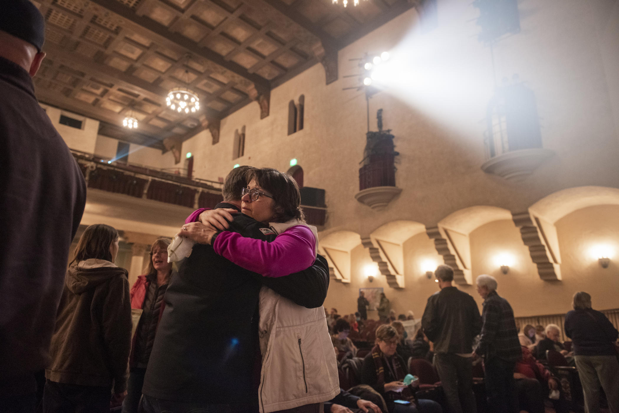 President Gayle Hutchinson shares a somber hug with someone as light shines through smoky air inside of Laxson Auditorium at a Camp Fire meeting.