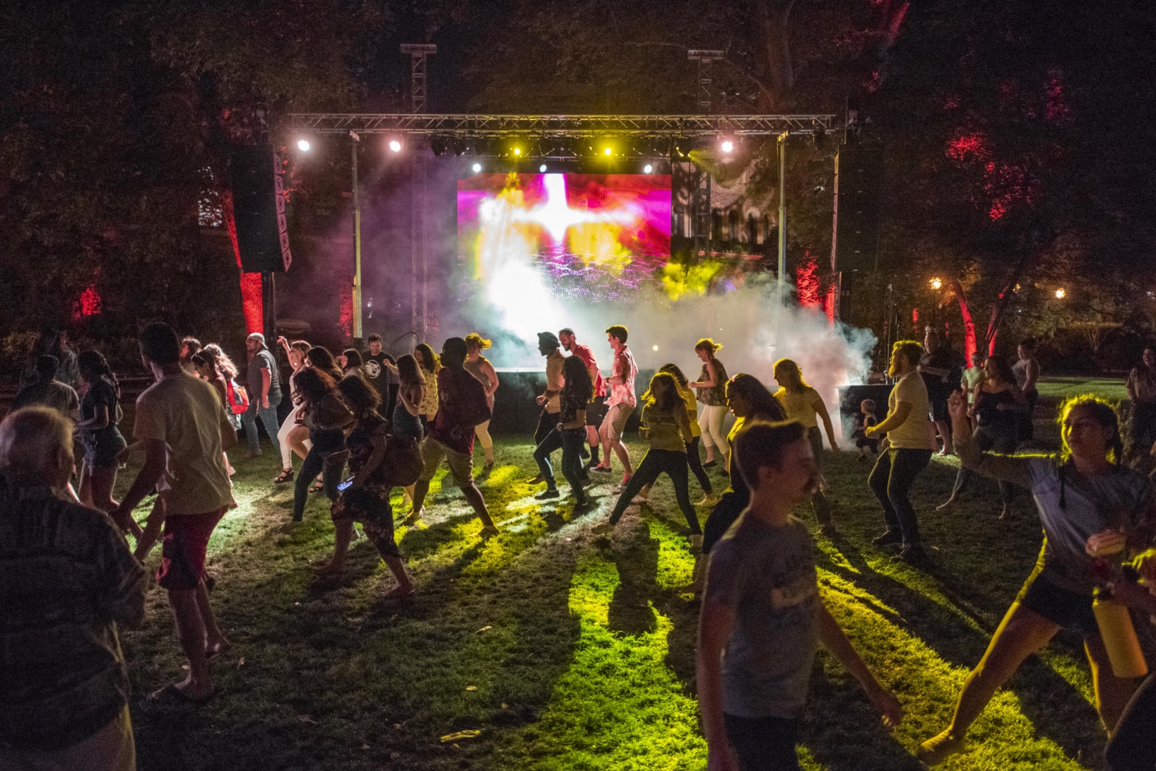 A large crowd of people dance in front of strobe lights and a smoke machine on Kendall Lawn.