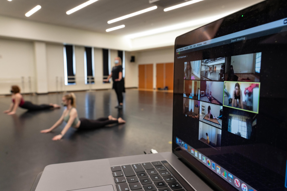 Students dance on a screen via Zoom as other students dance in a classroom.