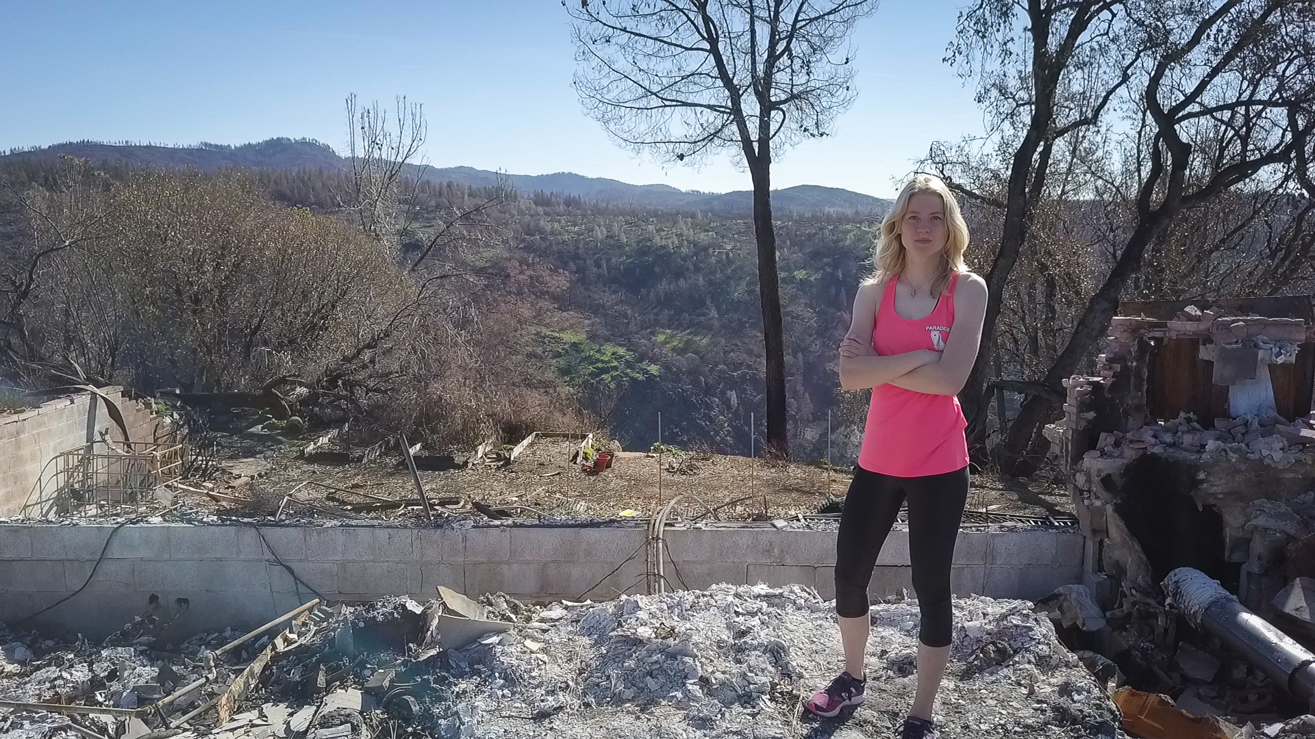 Wearing workout clothes, Cheyenne stands with her arms crossed in the ashes of her family home.