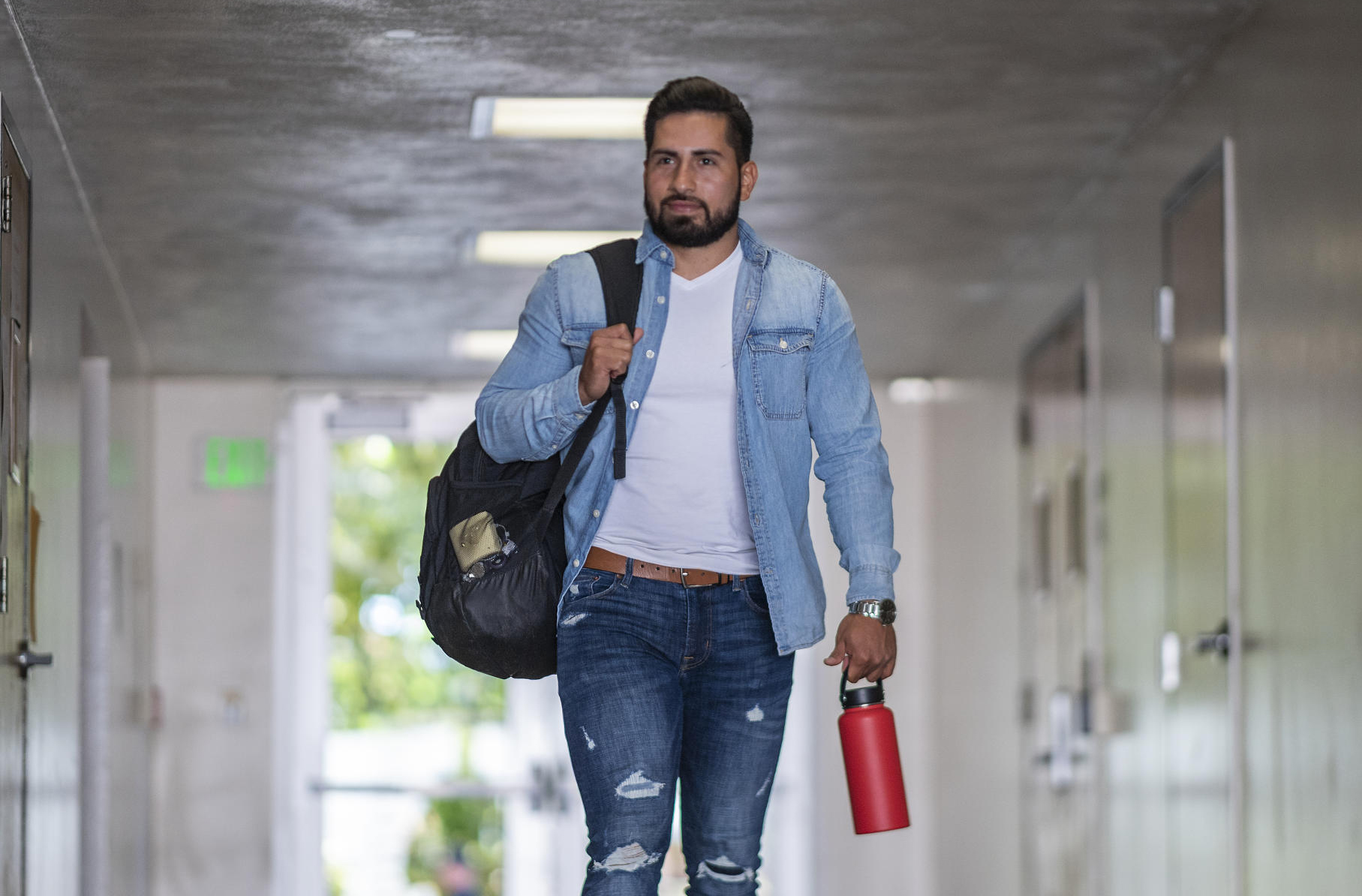 Jaime Valdovinos walks through an outdoor hallway on campus carrying his back and reusable water bottle