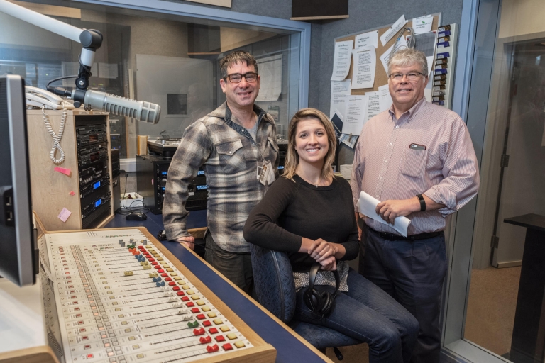 Three NSPR employees sit in a news studio among radio equipment.