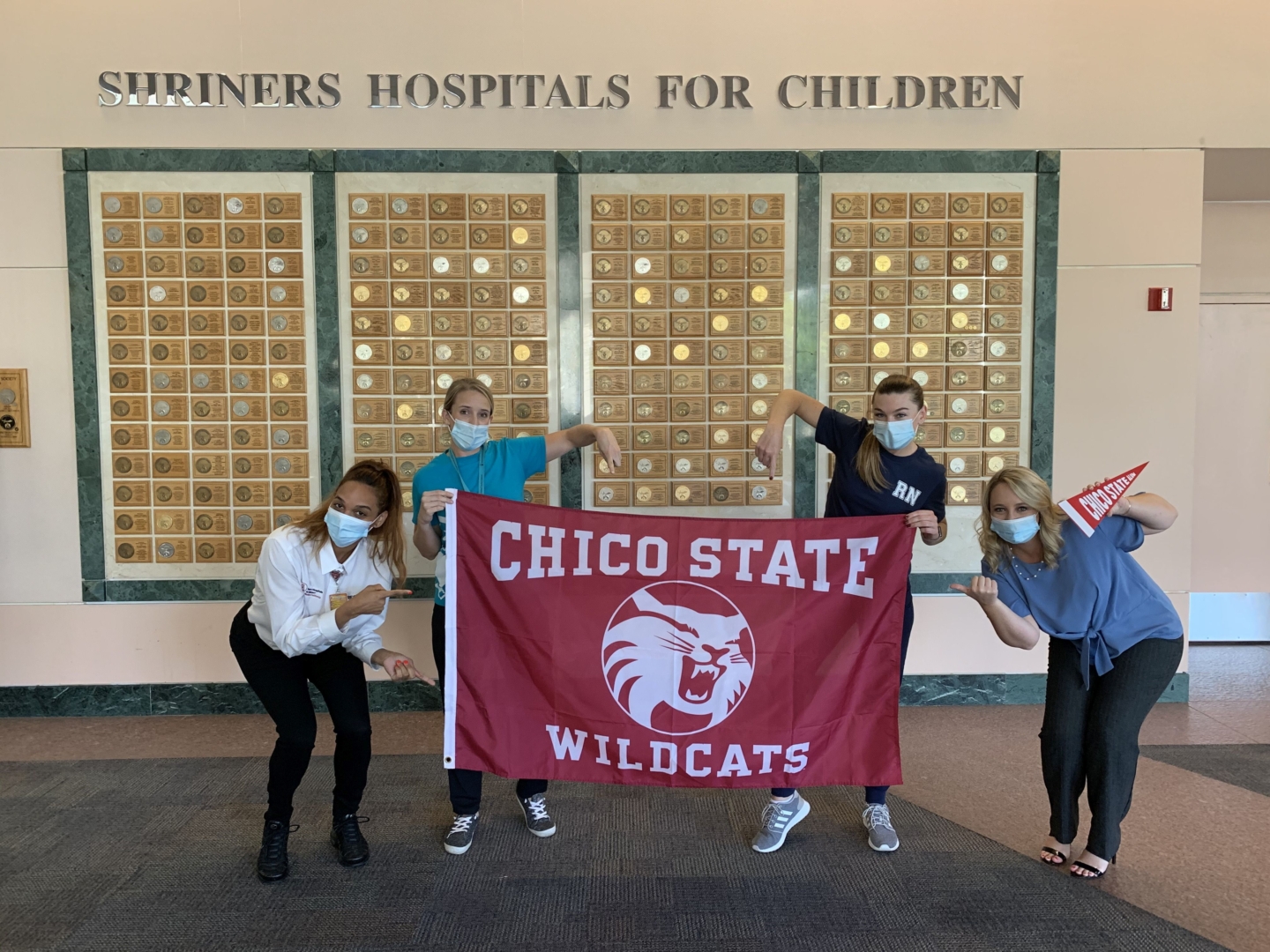 Four masked women pose with a Chico Sate Wildcats flag at Shriners Hospital