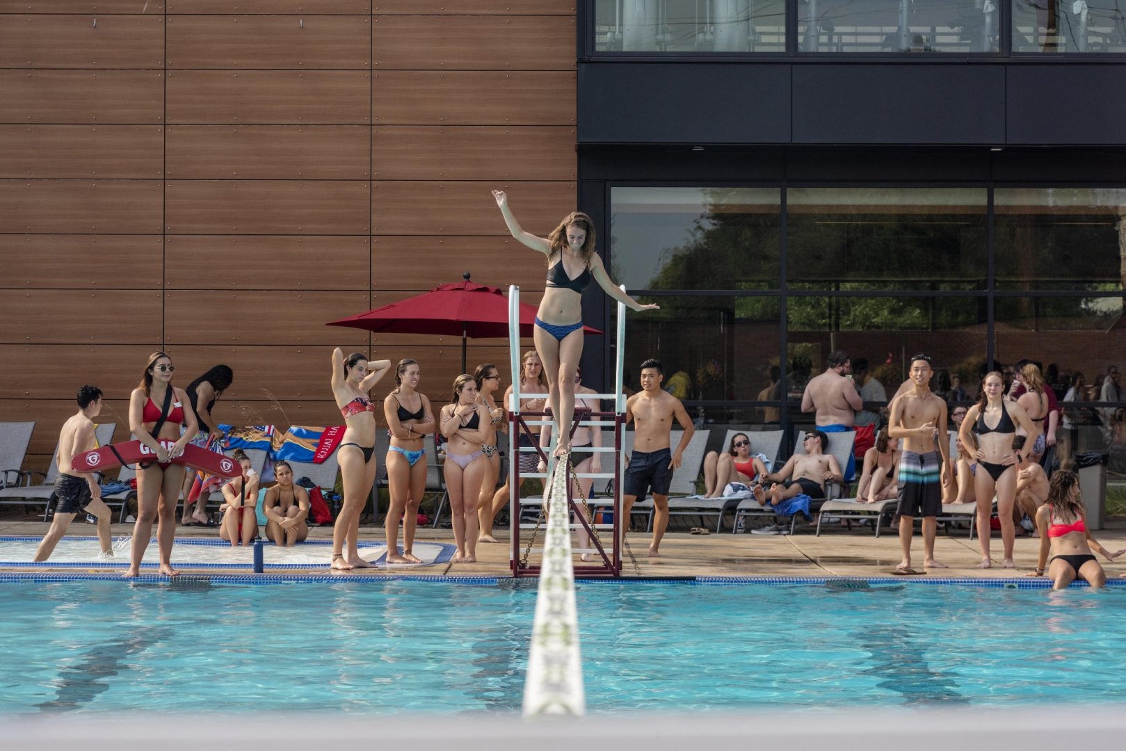 A student balances on a slackline that's crossing a pool as a group of students watches.