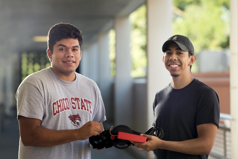 Two students smile and together hold a knee brace prototype.